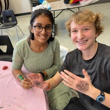 Two students smiling and one showing off the Henna done on their hand