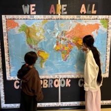 Two students looking at a world map hung on the wall